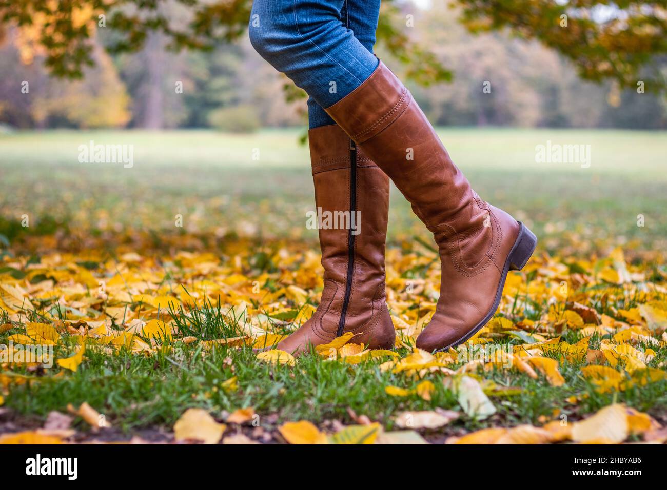 Woman wearing brown leather boot and walking in fallen leaves. Fashion model in autumn park Stock Photo