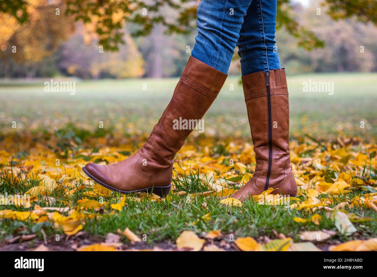Woman wearing brown leather boot and walking in fallen leaves. Fashion model in autumn park Stock Photo