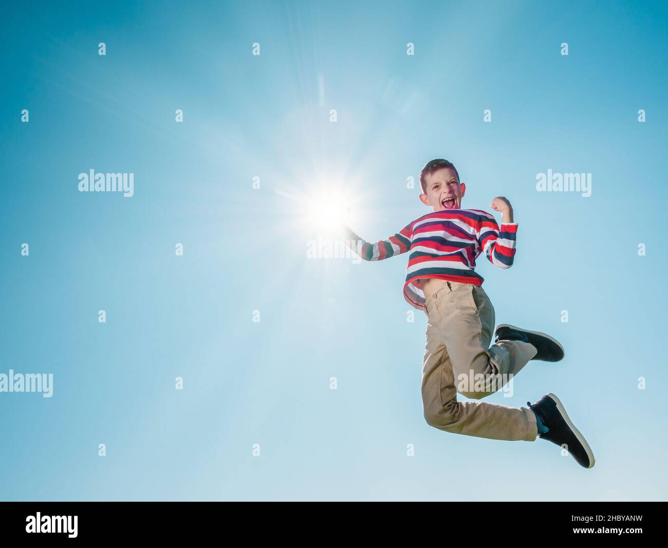 7 year old boy jumping so high and pretending to touch the sun with his right hand, isolated outdoors, active life and freedom concept Stock Photo