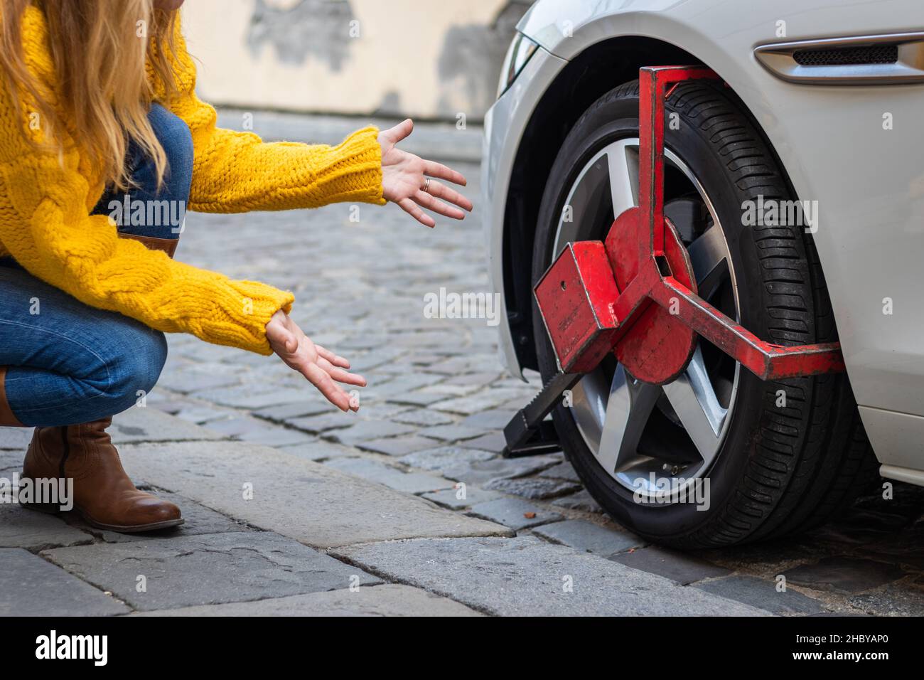 Upset woman looks at her parked car with wheel clamp. Punishment for illegal parking at street. Stock Photo