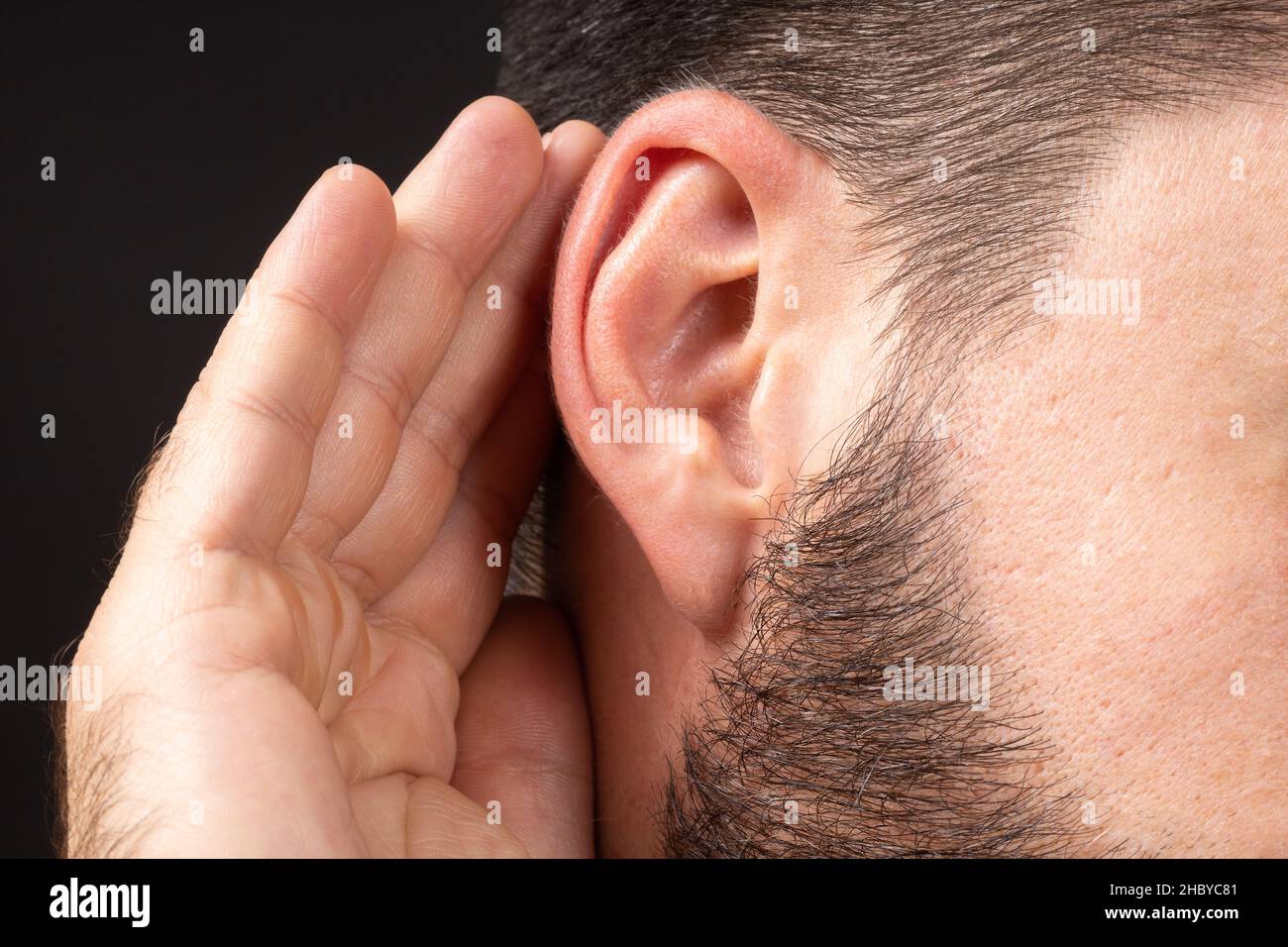 Close-up of man ear with palm listening and collecting rumors. Concept of secret or sense organs, hearing. Stock Photo
