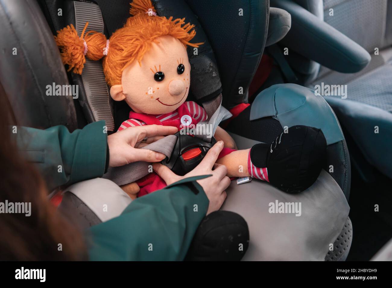Female's hands fasten the seat belts on a plush doll sitting in a child