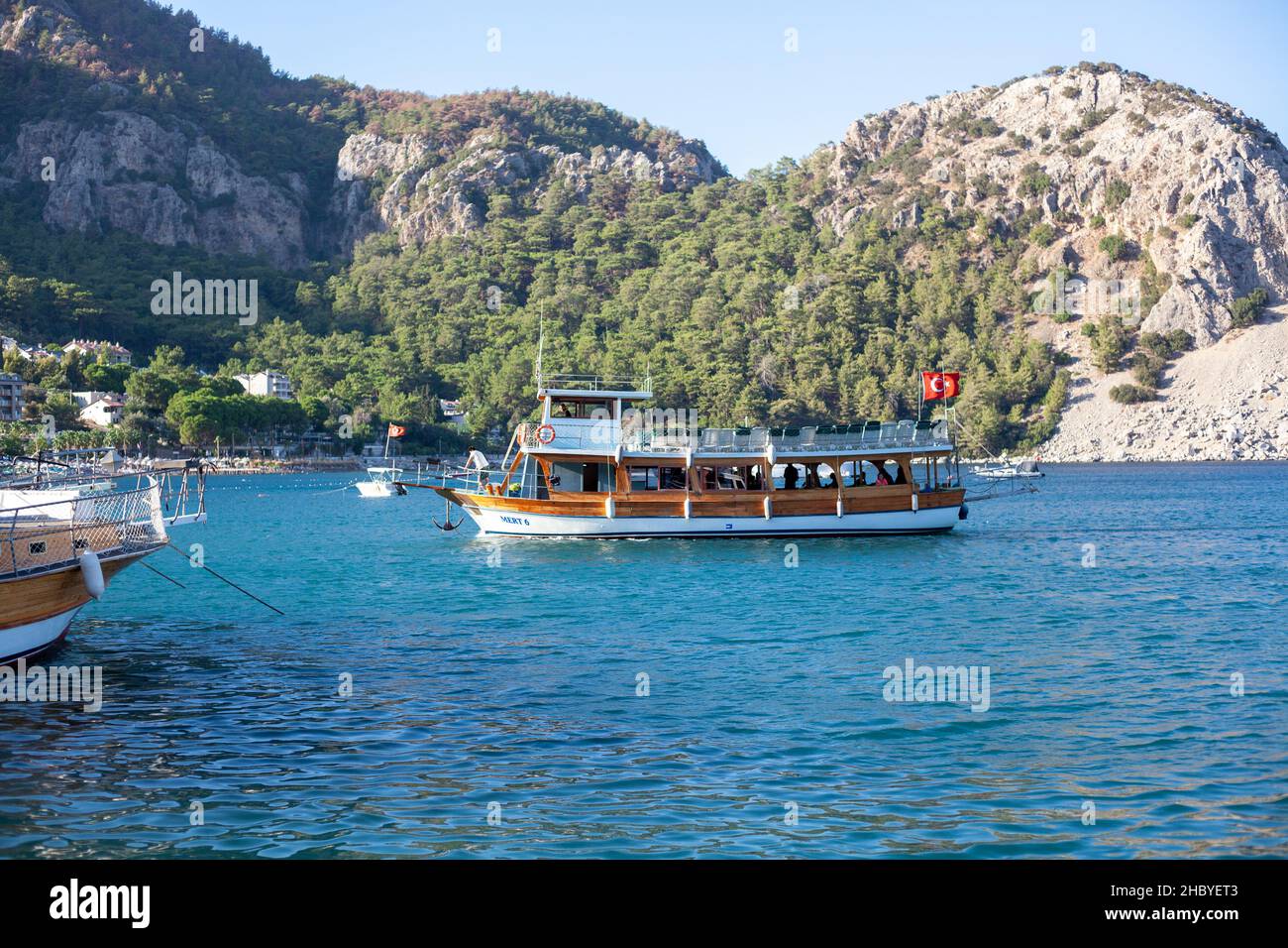 Sea water taxi boat arrives at the port. Sea bay surrounded by mountains and rocks in small touristic village Turunc. Turunc, Turkey - September 4. 20 Stock Photo