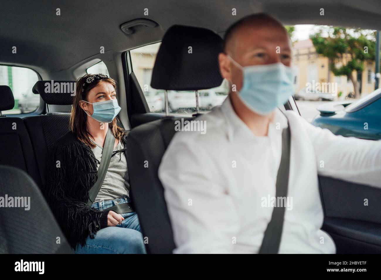 Taxi driver in a mask with a female client on the back seat wearing mask Stock Photo