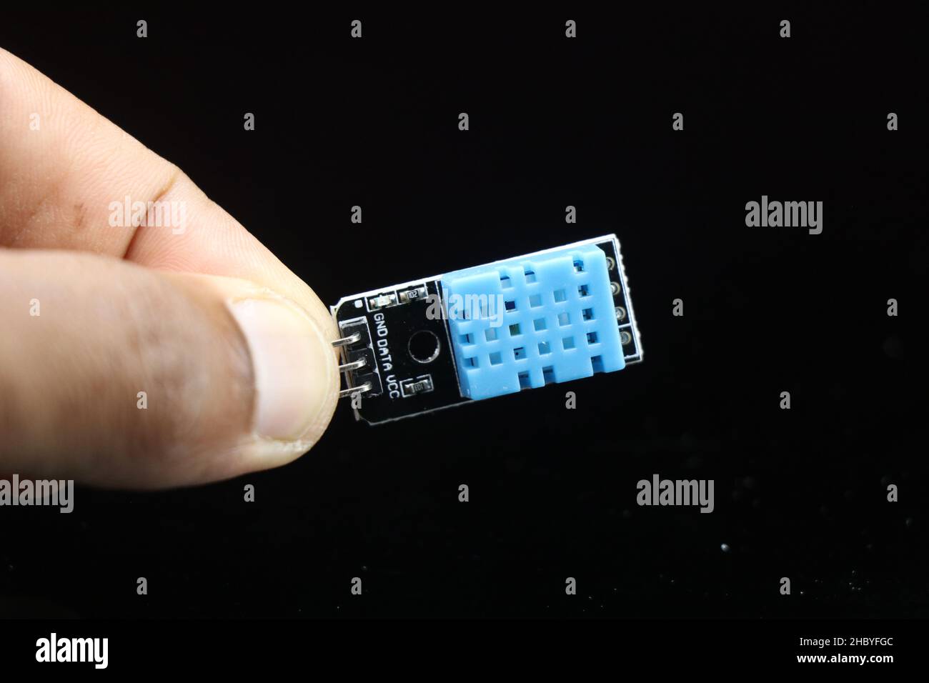 Temperature and humidity sensor module or DHT11 board held in hand isolated on black background Stock Photo