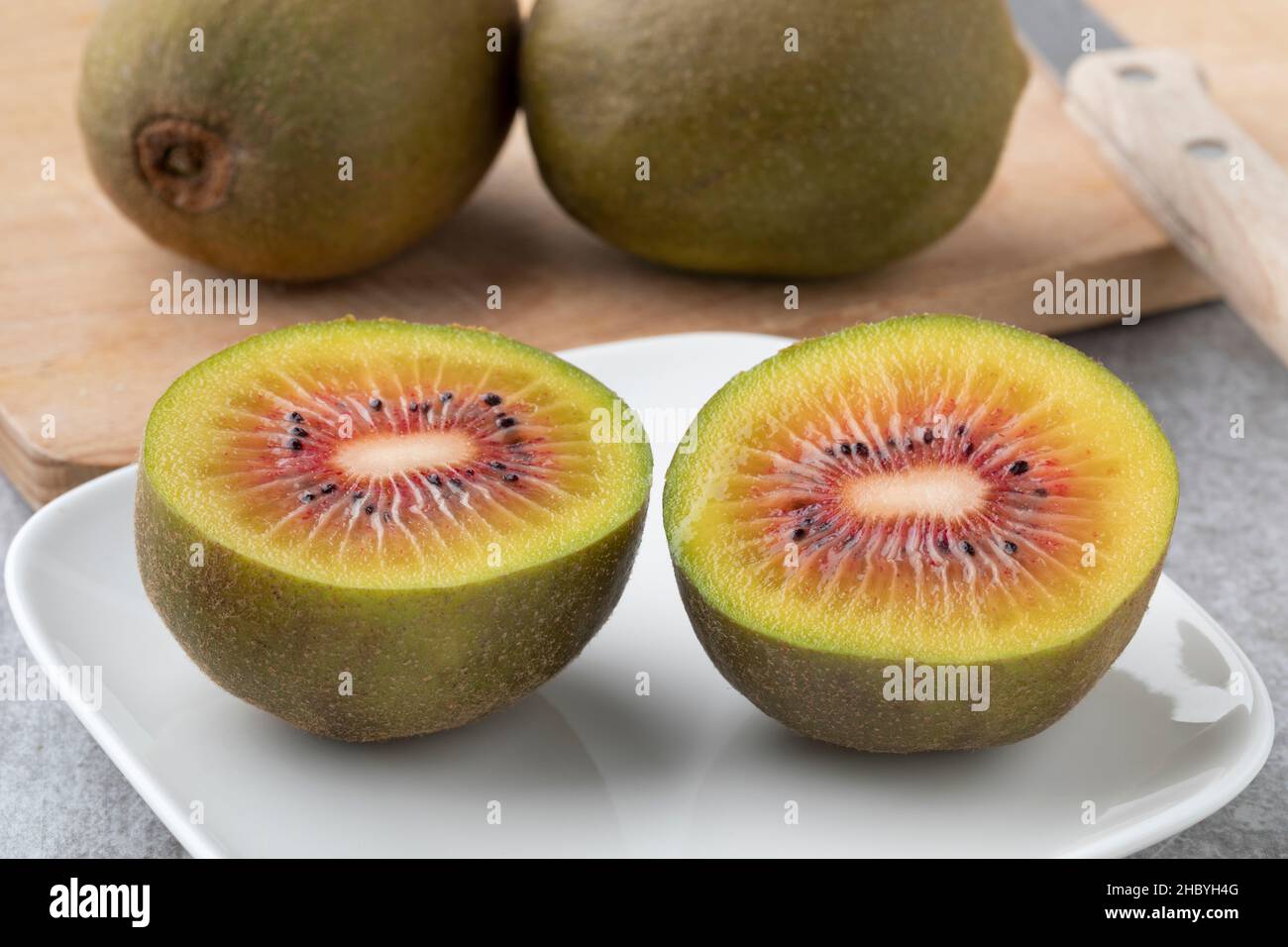 Fresh halved sweet red kiwi on a plate close up and whole ones in the