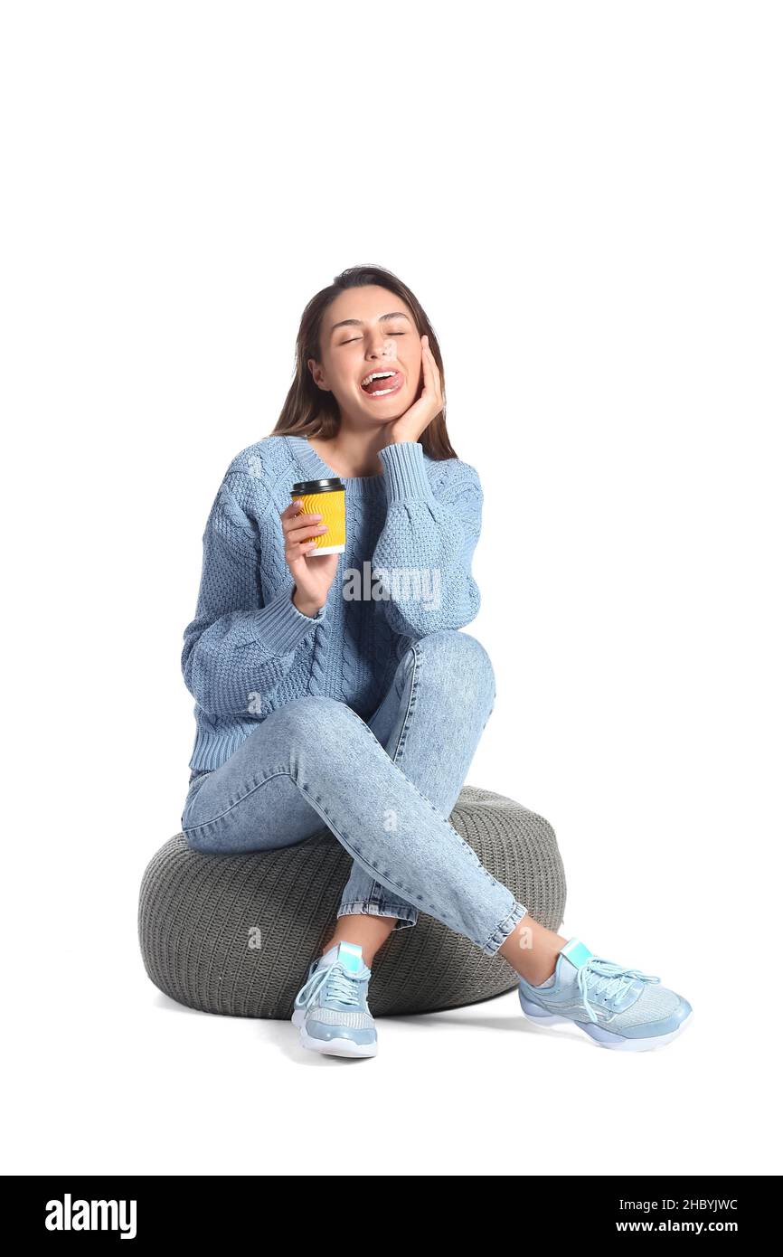Beautiful woman with cup of coffee sitting on pouf against white ...