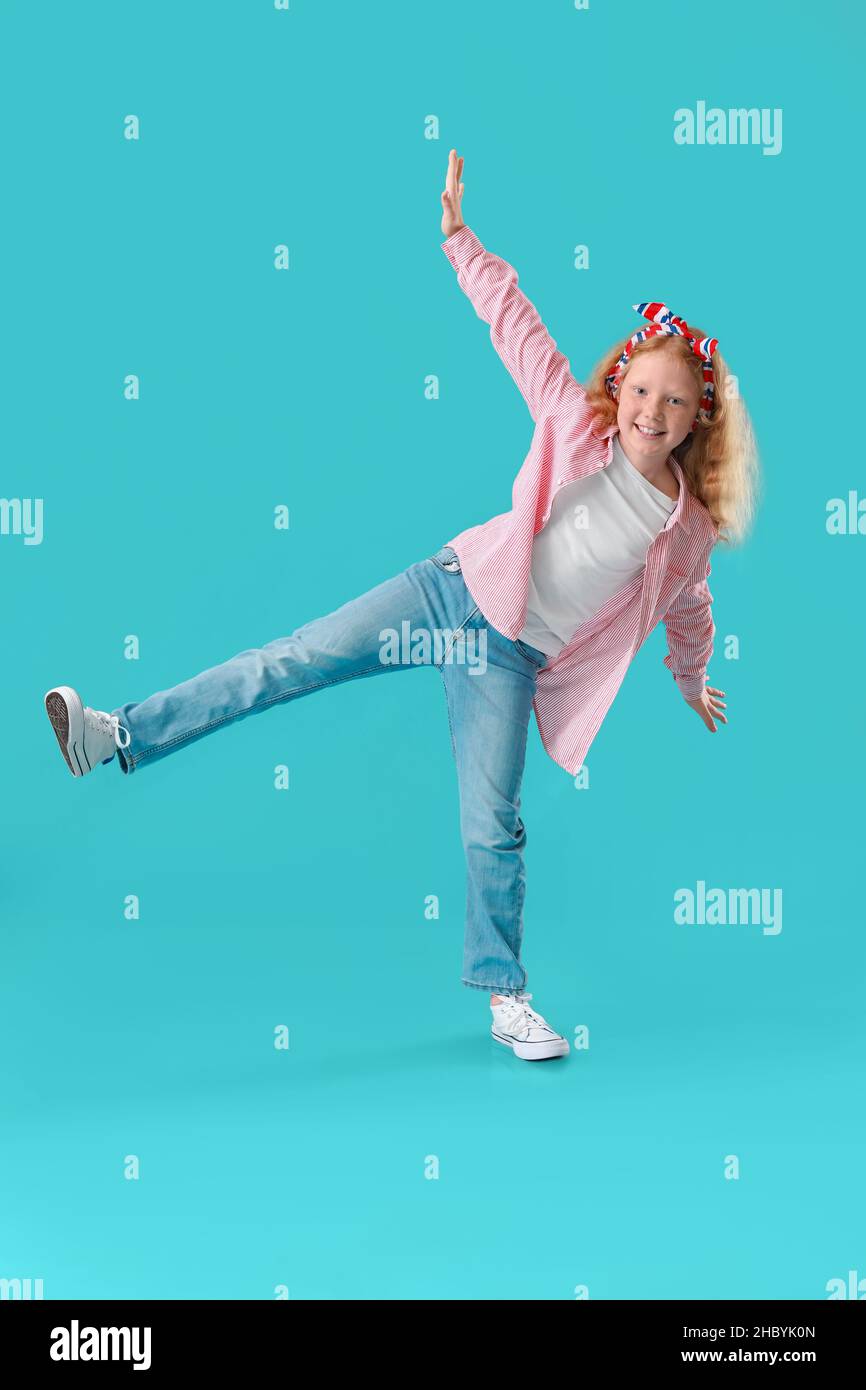 Little redhead girl in striped shirt dancing on blue background Stock