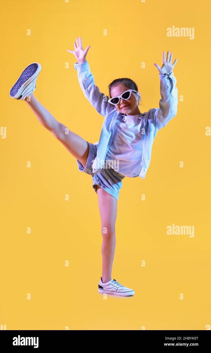 Adorable little girl in sunglasses dancing on yellow background Stock