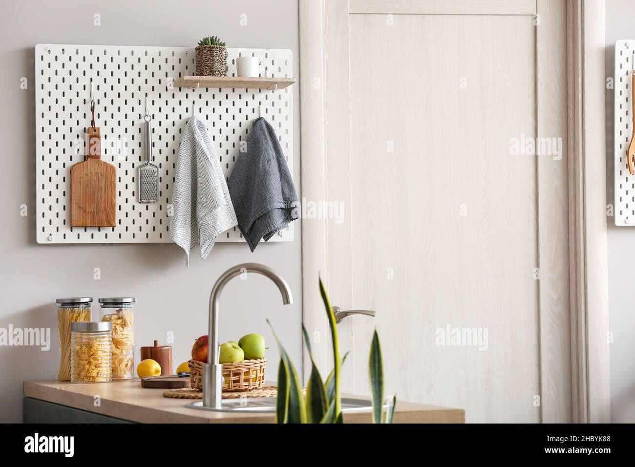Peg board with kitchenware hanging on light wall Stock Photo