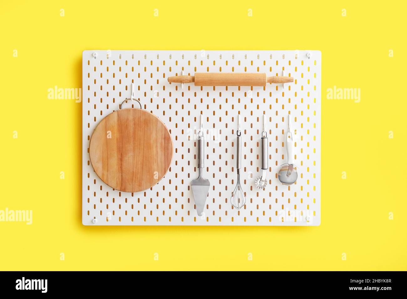 Peg board with kitchenware hanging on yellow wall Stock Photo