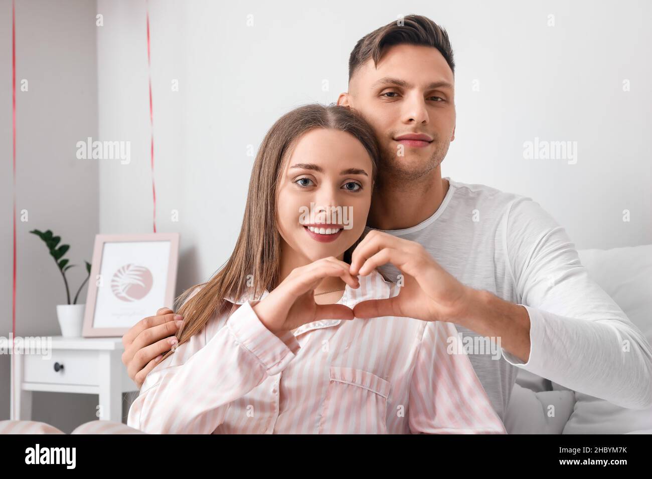 Happy couple making heart shape with their hands in bedroom. Valentine ...