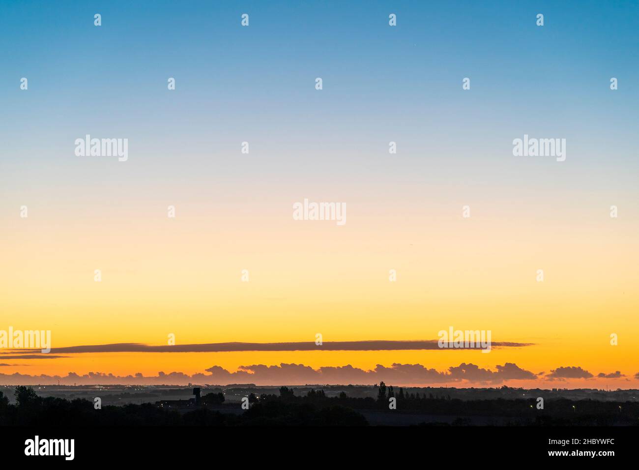 Wide angle view of the dawn sky over the kent landscape with lowe level cumulus clouds formed into cloud streets on the horizon. Clear sky above. Stock Photo