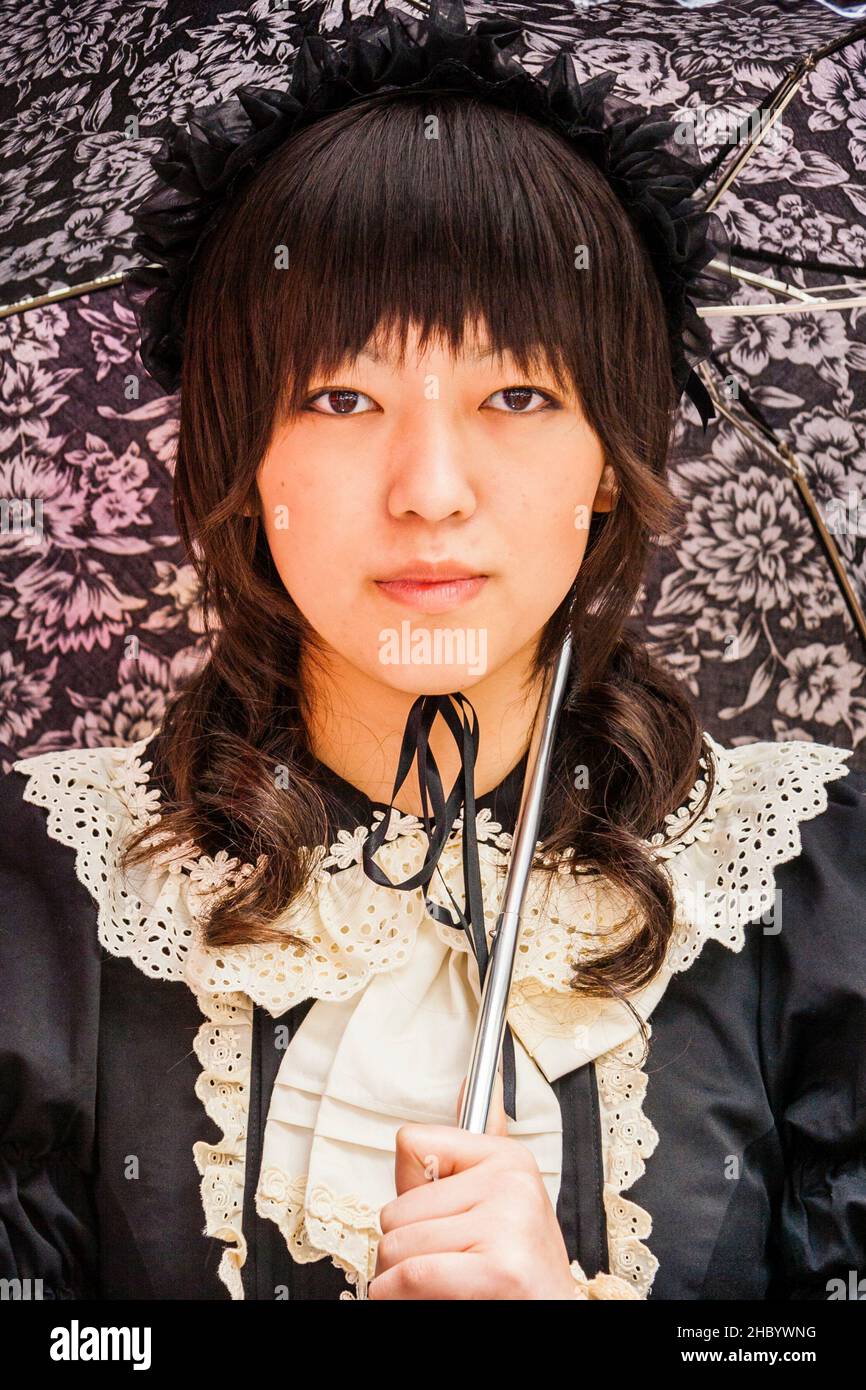 Tokyo, Harajuku. Cosplay. Close up portrait of young Japanese woman in Classic Gothic Lolita style clothing with umbrella, looking directly at viewer. Stock Photo