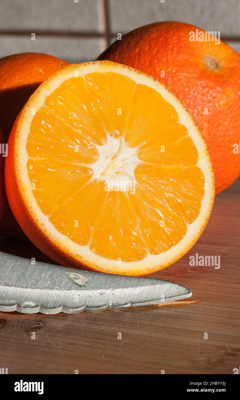close-up of an orange cut  in half with a knifeon a wooden table Stock Photo