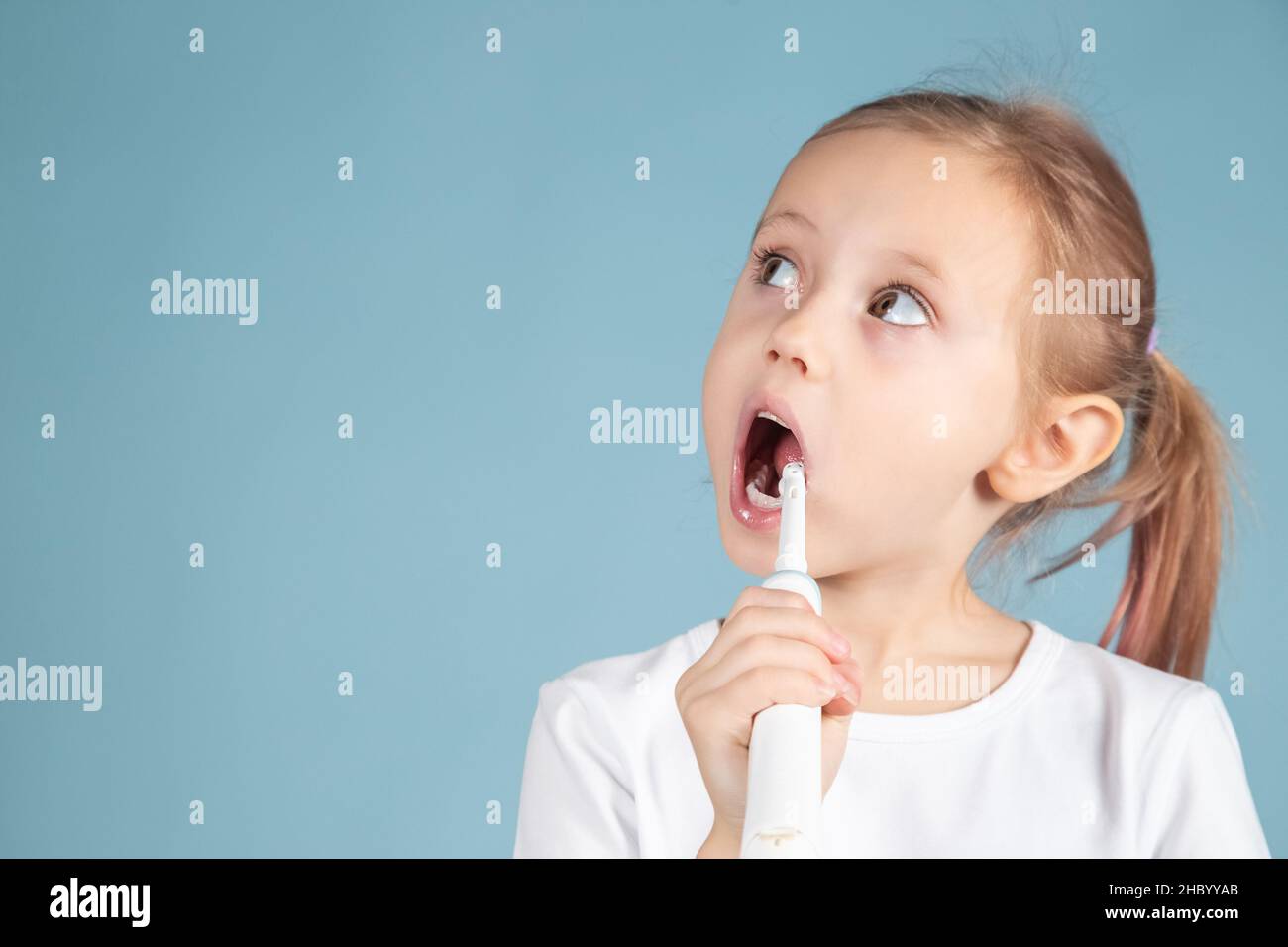 Adorable little caucasian child brushing teeth Standing Over blue Background Stock Photo