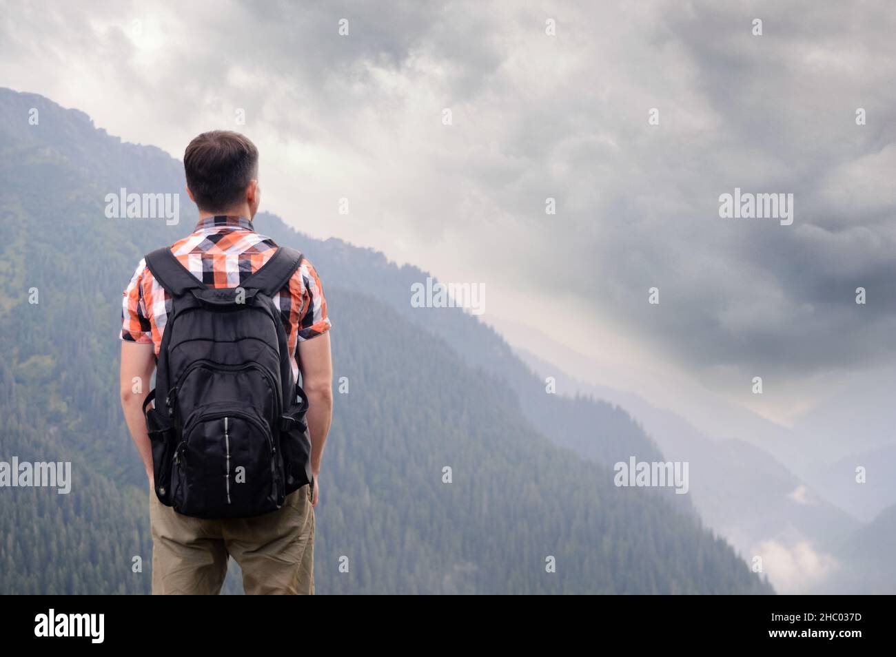 A tourist with a backpack stands alone in the mountains and sees a dark stormy sky. The concept of air pollution, environmental problems, the crisis o Stock Photo