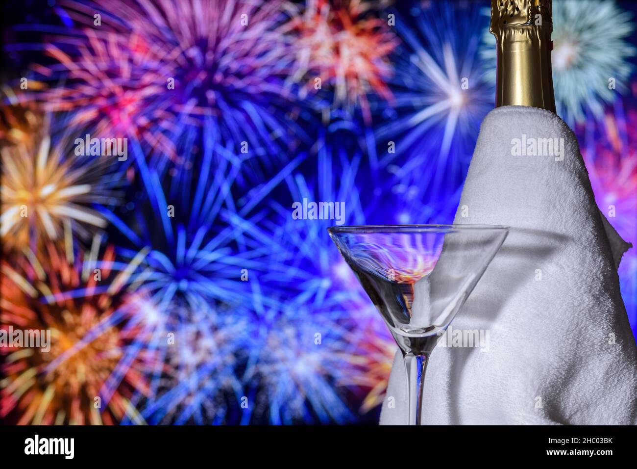 Festive glass with a bottle of champagne against the background of blurry fireworks lights during the celebration of the New Year. Stock Photo