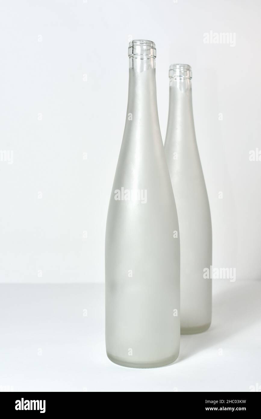 two empty wine bottles without labels standing on a table against a white background Stock Photo