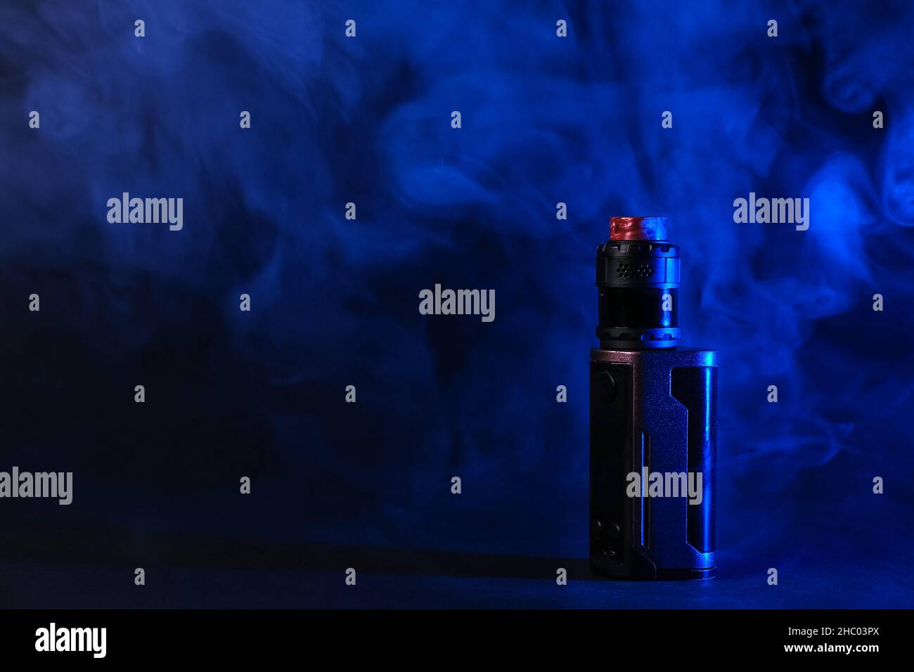 Electronic vaping device mod, atomizer stands in vape smoke and vapor illuminated by blue light. Stock Photo