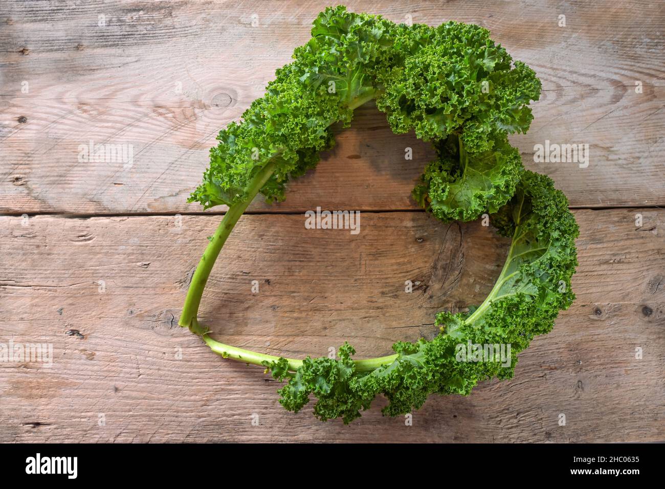 Curly leaves of kale or green leaf cabbage in the shape of a heart on a rustic wooden table, healthy winter vegetable with vitamins, fiber and mineral Stock Photo
