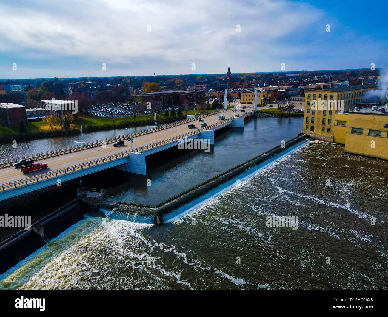 Bridge with cars goes over flowing water with city buildings on bright day Stock Photo