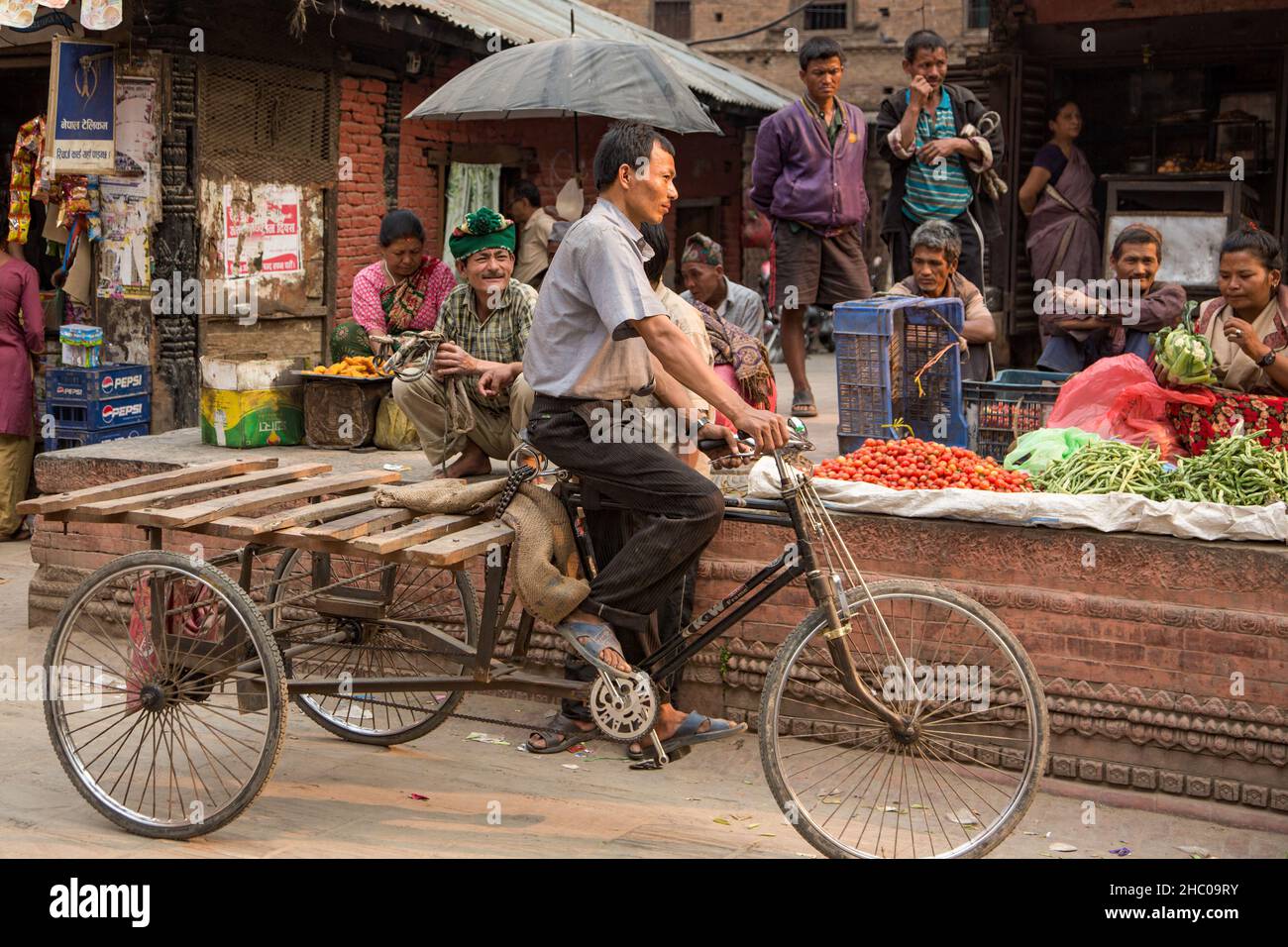 A Nepali man pedals a threewheeled tricycle cart past vendors selling