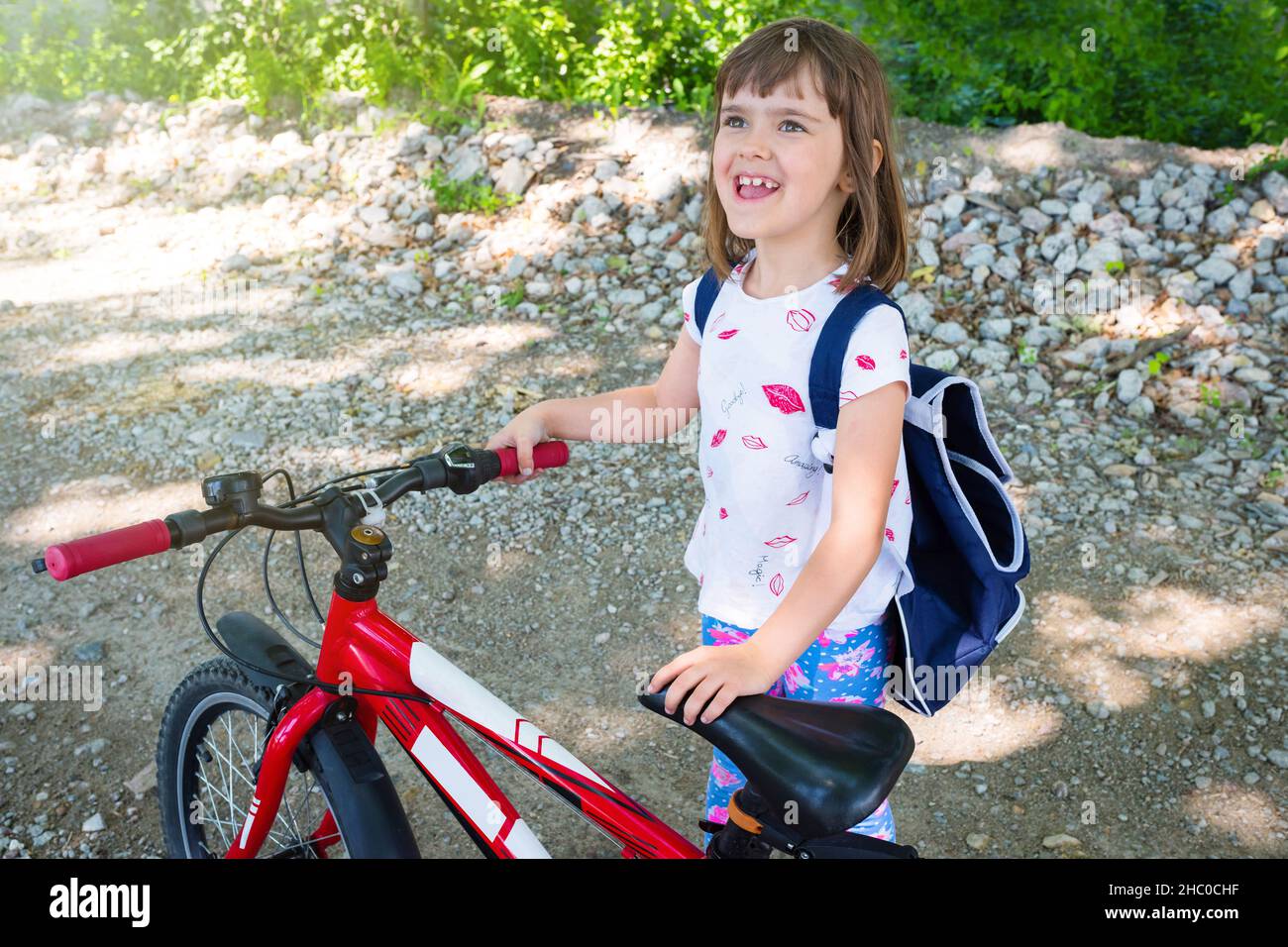 A portrait of a happy child with a backpack and bike on the street. Stock Photo