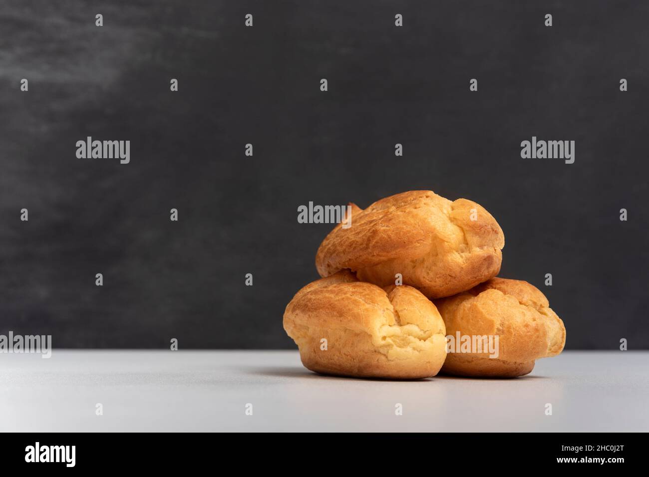 Profiteroles or popovers, eclairs side view. Three appetizing profiteroles. Gray background Stock Photo