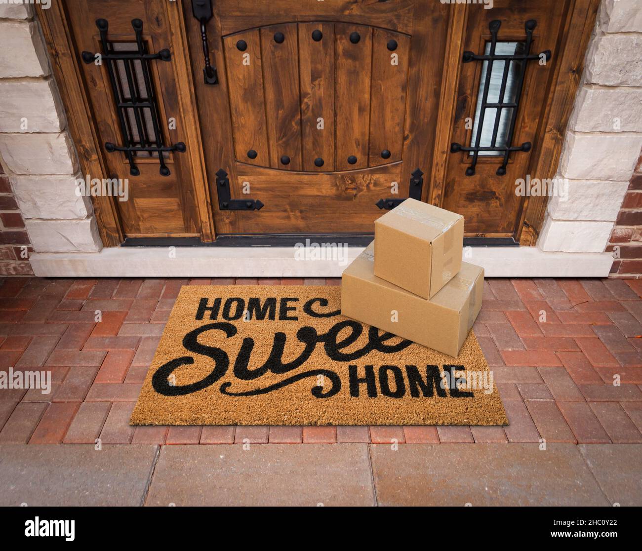 Small Packages Sitting on Home Sweet Home Welcome Mat At Front Door of House. Stock Photo