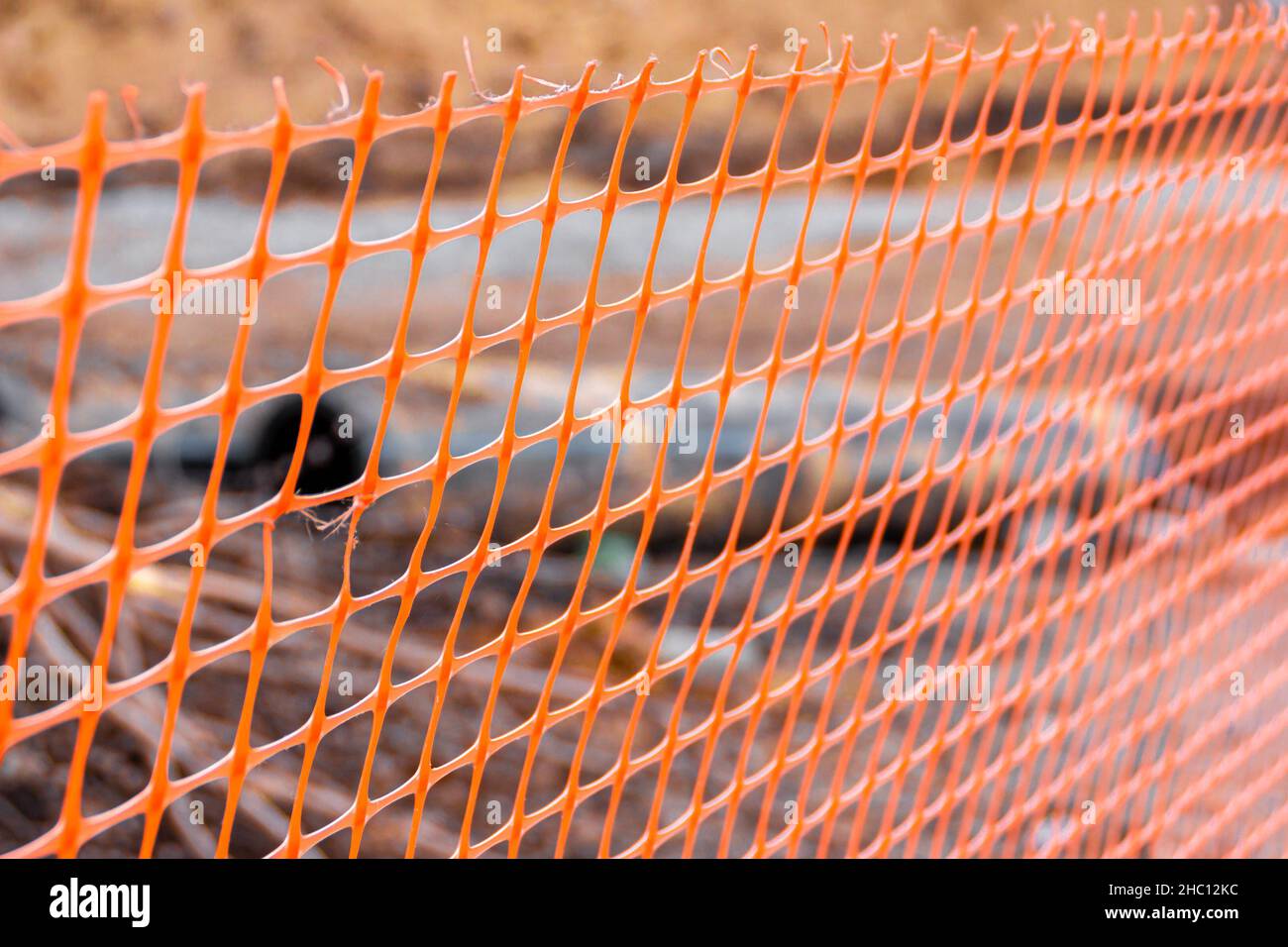 Emergency fencing orange plastic mesh behind which excavation works and pipe laying of underground utilities are carried out, selective focus Stock Photo