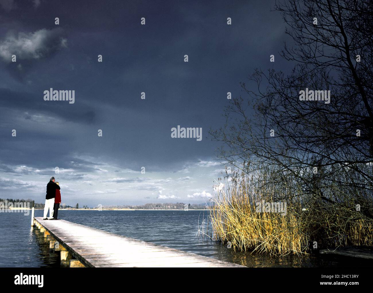 Man & Woman standing  on a small short wood  pier, jetty, Chiemsee, Bavaria,  Germany Stock Photo