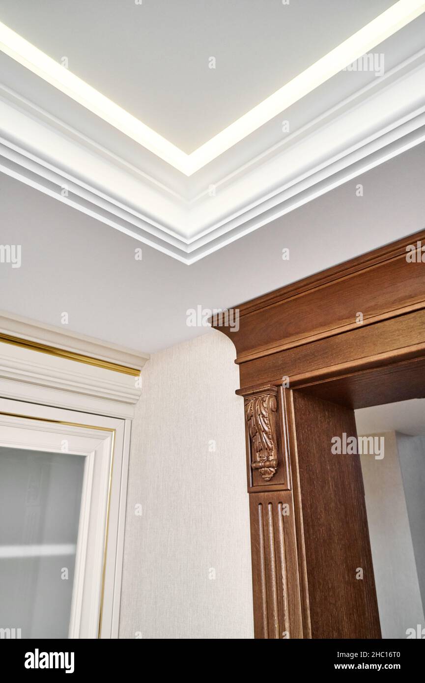 Decorated wooden doorway with carved furniture brackets and fluted panel in light spacious room with contemporary led backlight on ceiling Stock Photo