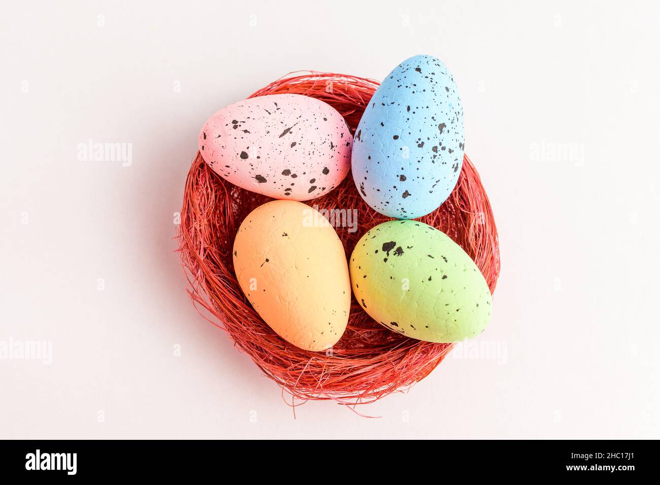 Mixed colored decorative red Easter eggs in a red rustic basket isolated on a white table Stock Photo