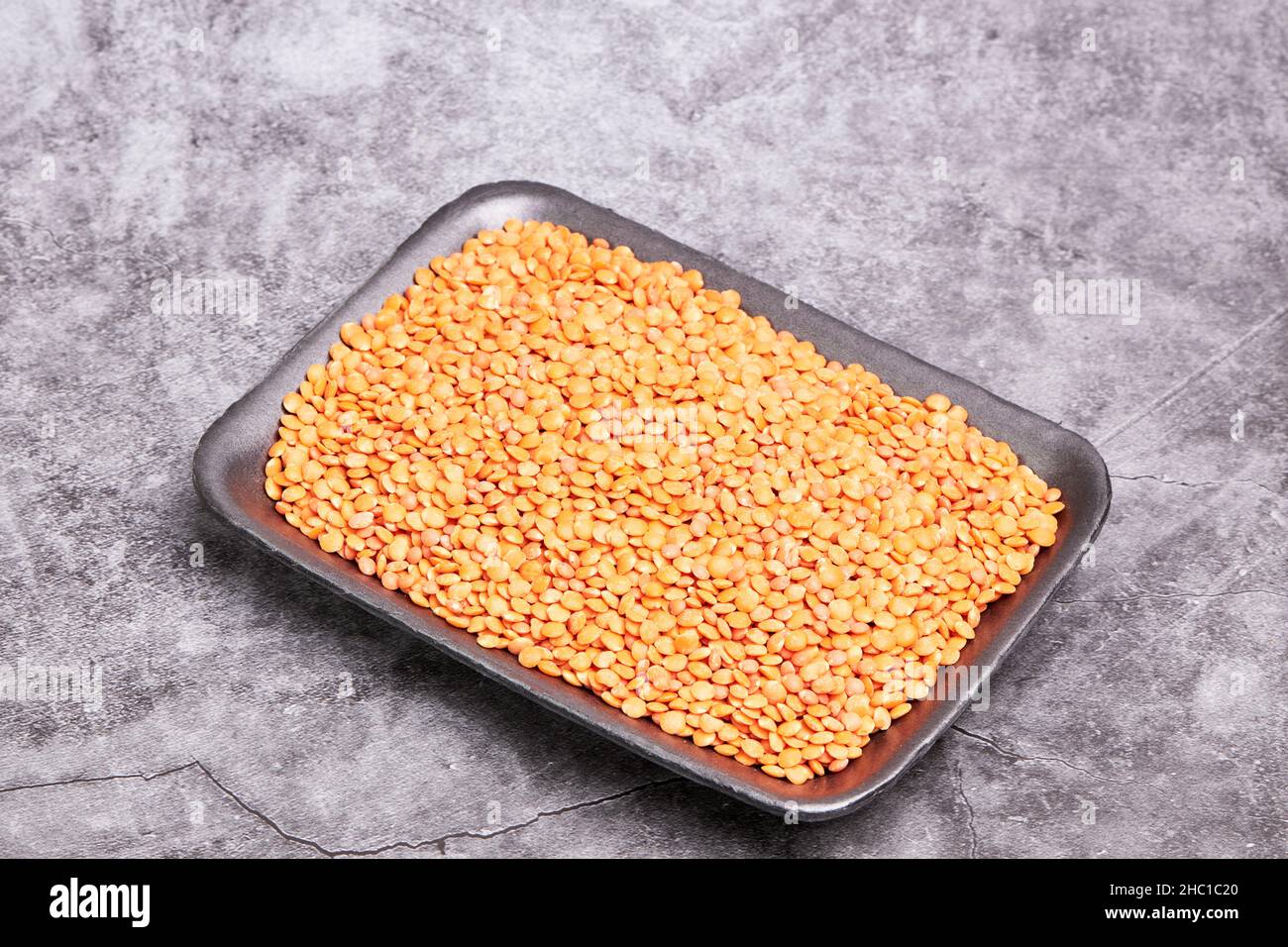 Black tray with raw orange lentils on a gray stone background. Healthy food concept Stock Photo