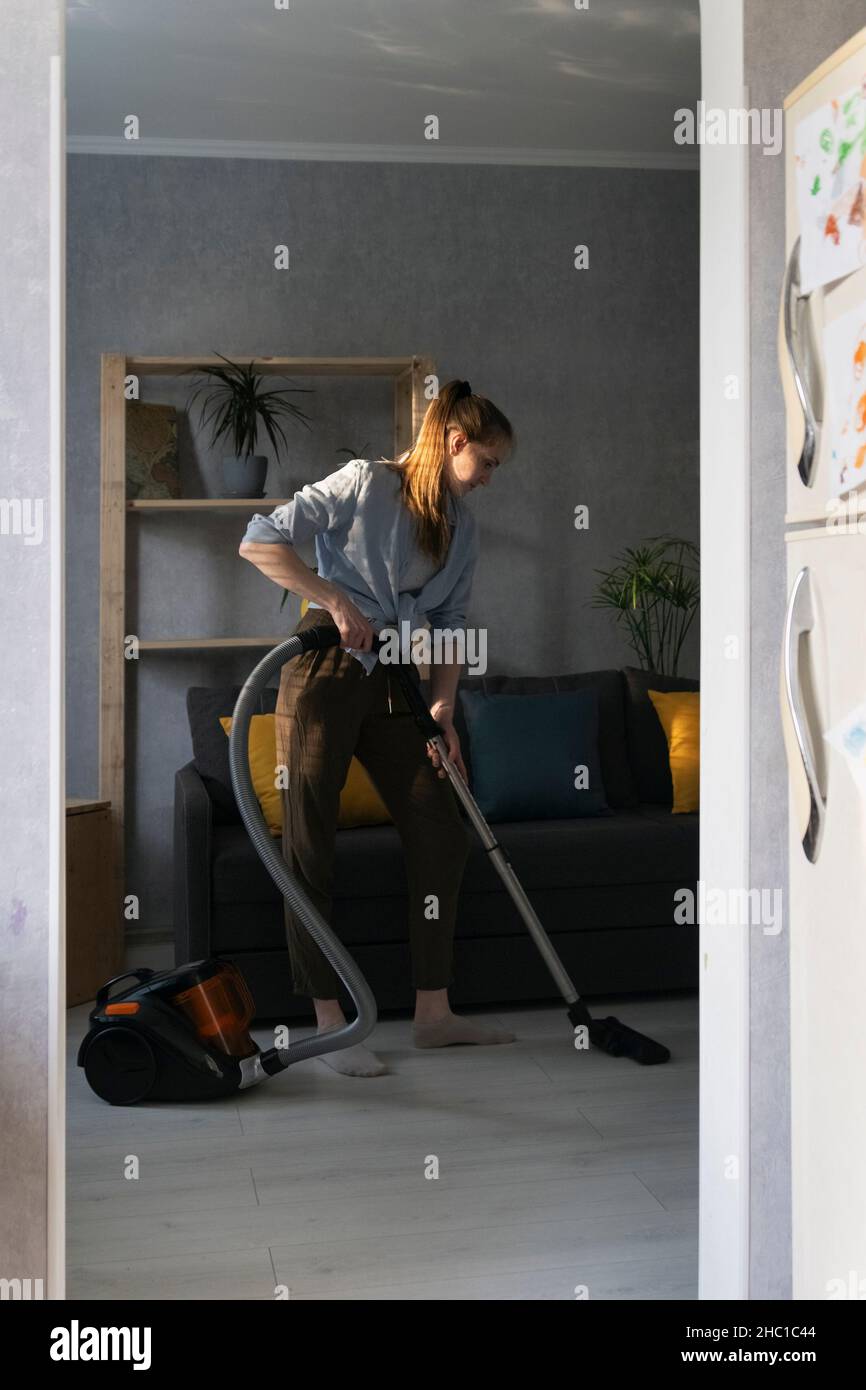 Young woman is cleaning the apartment with vacuum cleaner. Housekeeper ...
