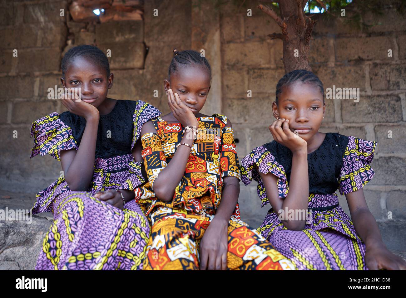 Three beautiful young welldressed black African girls sitting side by side in front of a wall with stern expressions on their faces, patiently waiting Stock Photo