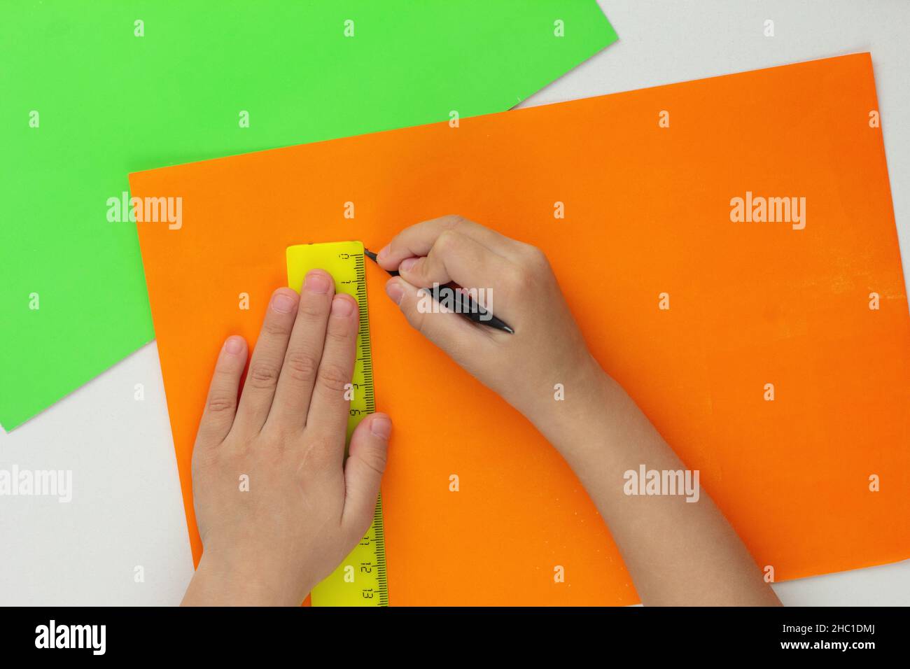 Top view of child hands drawing line using pencil and ruler on orange paper on white background Stock Photo