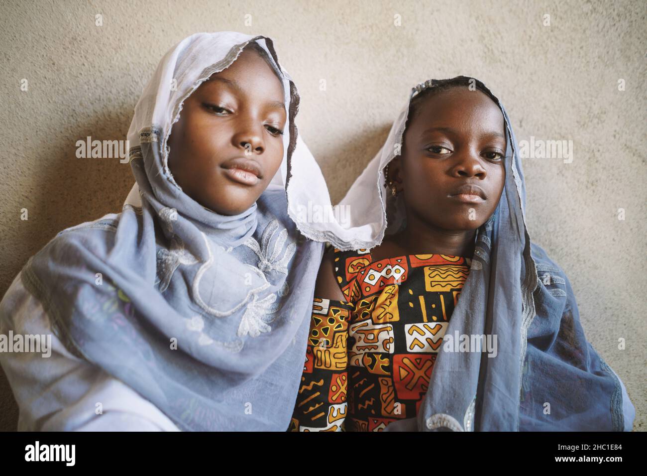Two mourning black African sisters who symbolically seek protection under their mother's scarf; dealing with grief in children concept Stock Photo