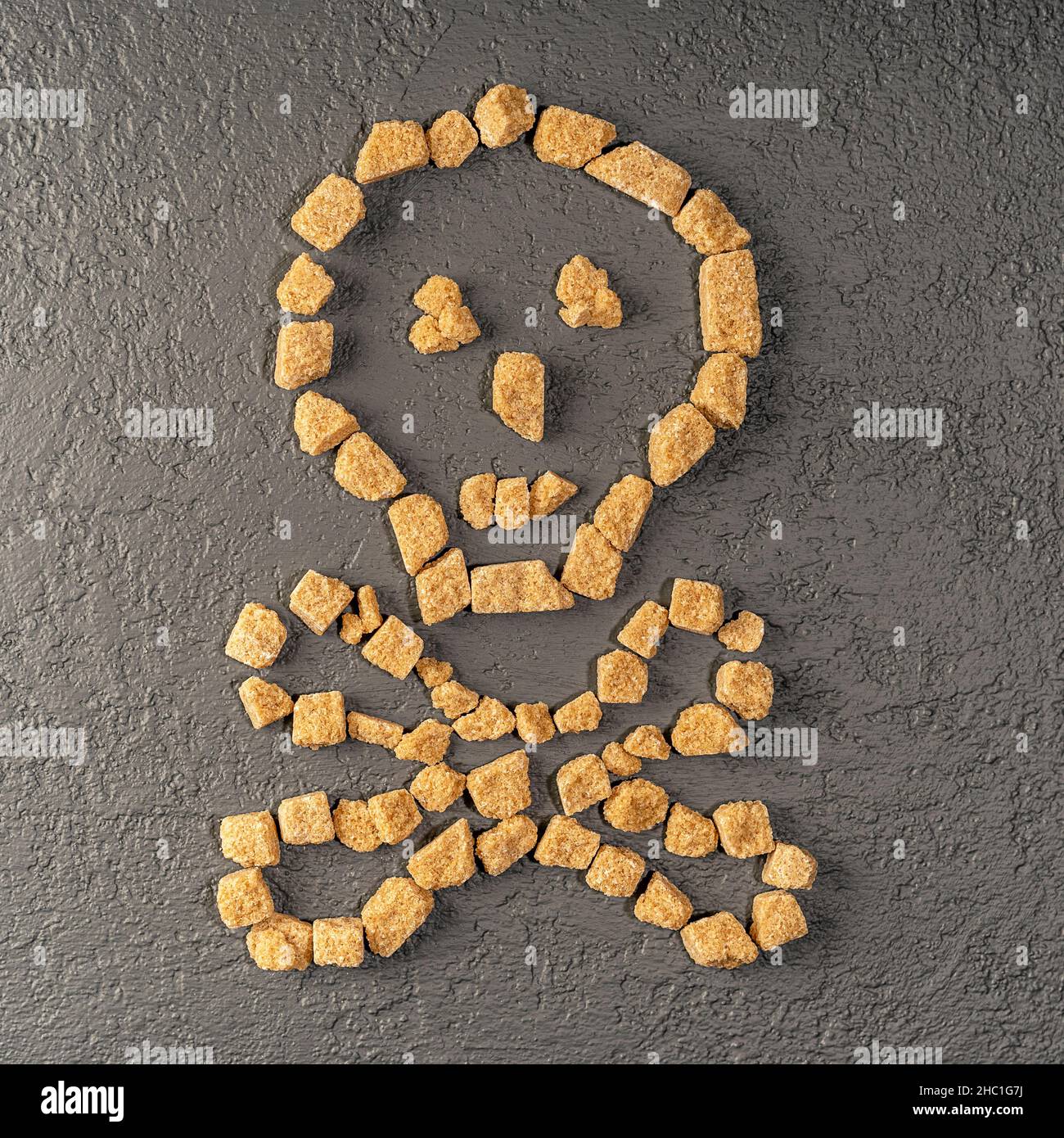 Cane sugar in the form of a skull and bones. Warning that sugar and sweets are dangerous to health. The skull is lined with unrefined sugar. Selective Stock Photo