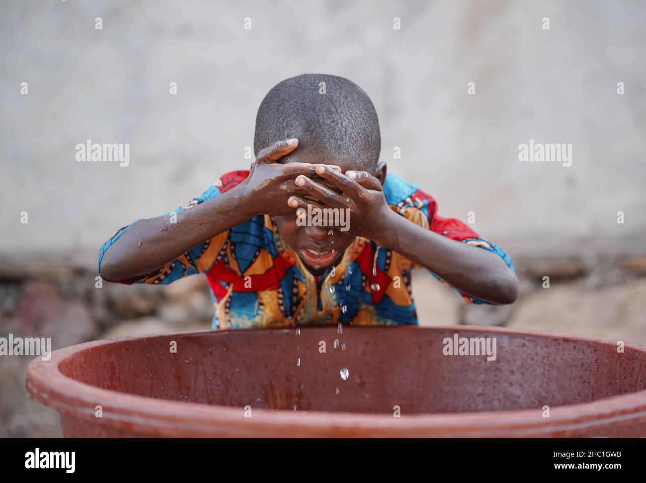 Little black African toddler rubbing his forehead with fresh and clean water from a plastic basin during his morning toilet Stock Photo