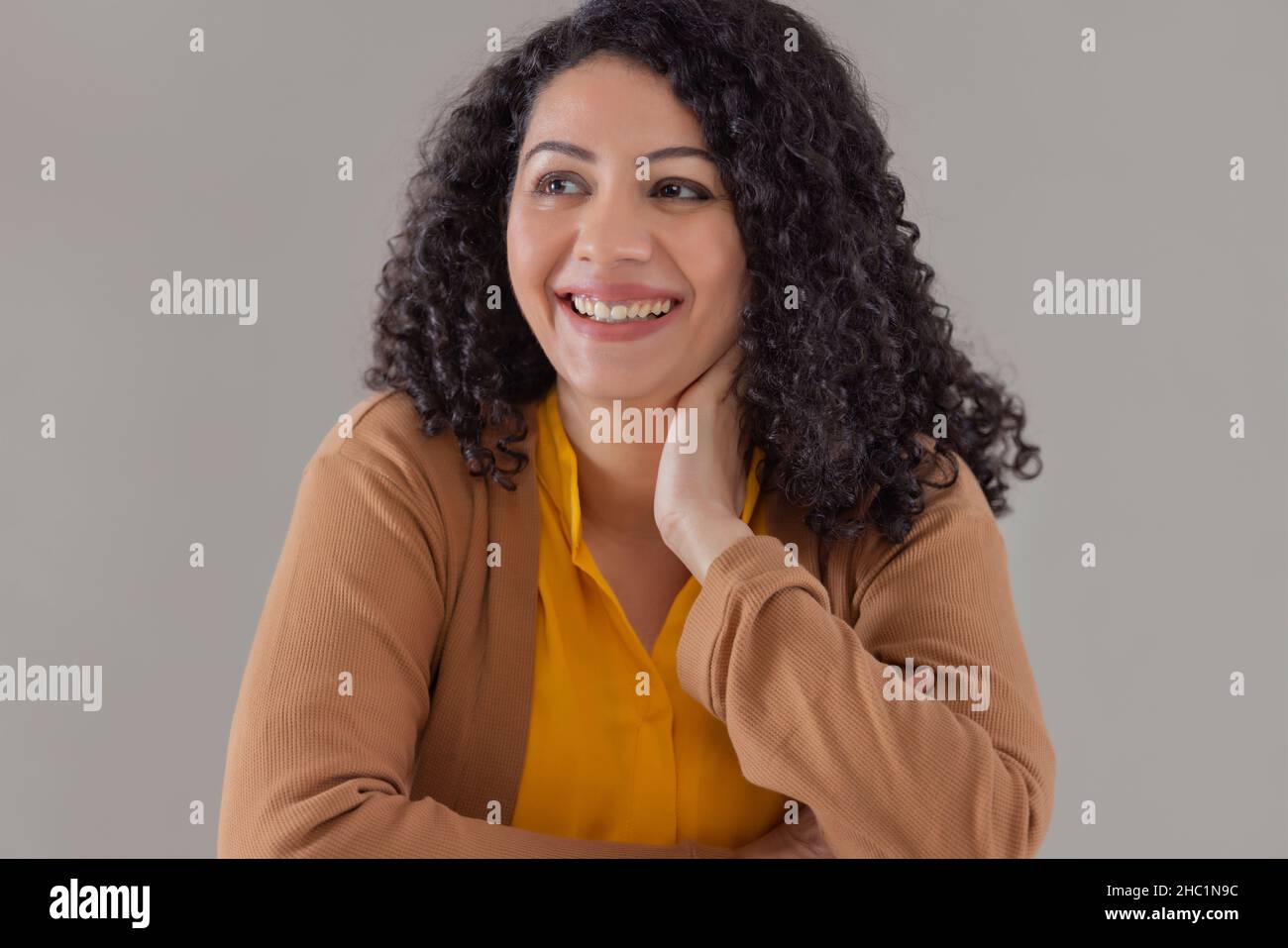 Happy adult woman sitting with hand on neck looking away with smile Stock Photo