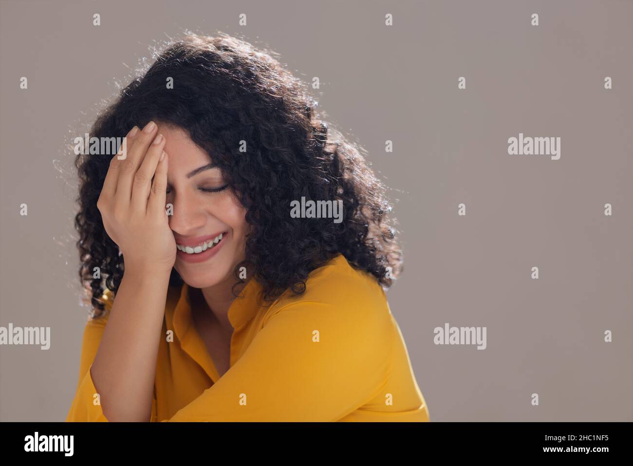 Portrait of a shy smiling woman covering her half face with hand with ...