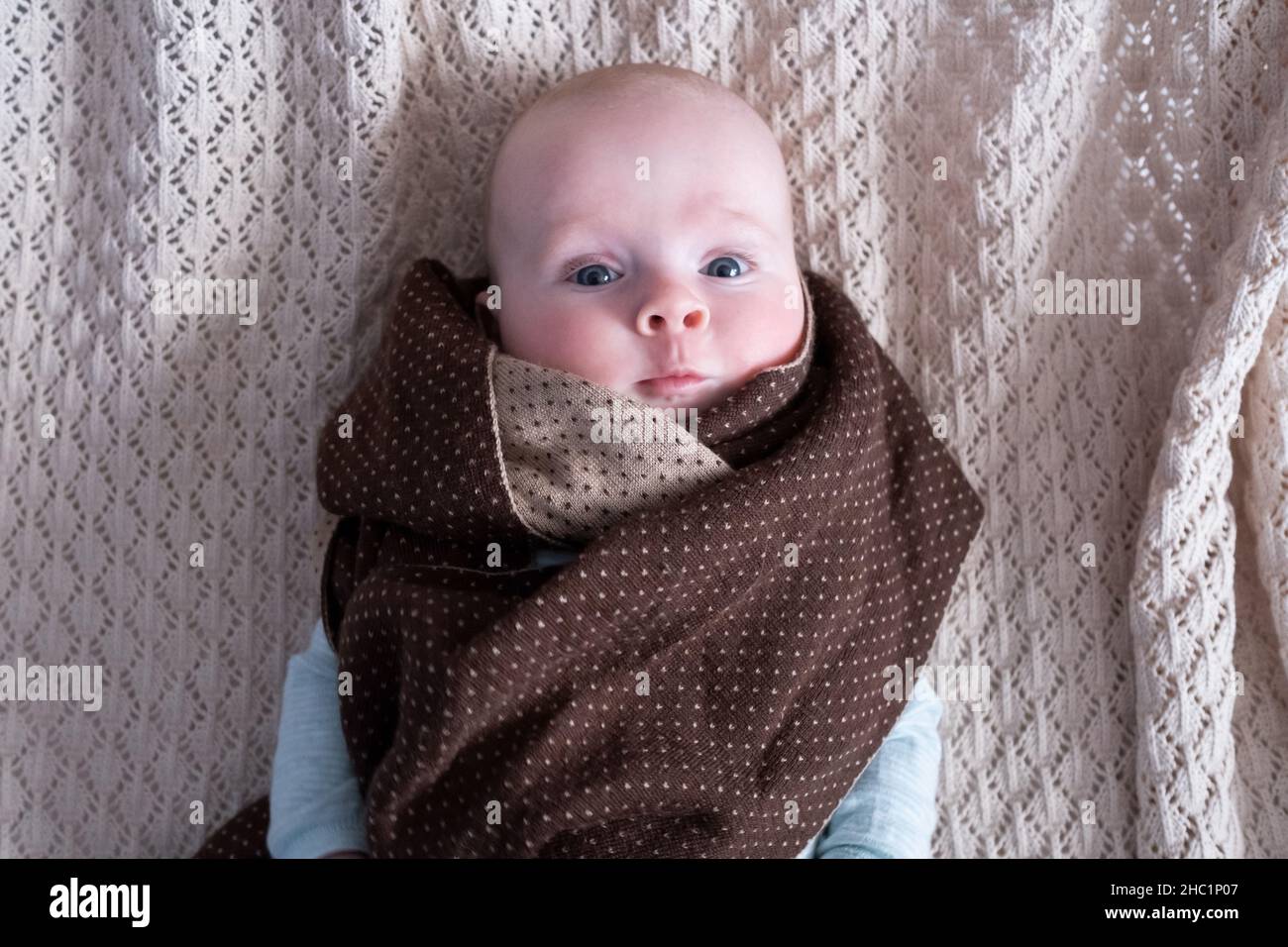 Cute baby with big blue eyes wearing a hat and a huge knitted scarf Stock Photo