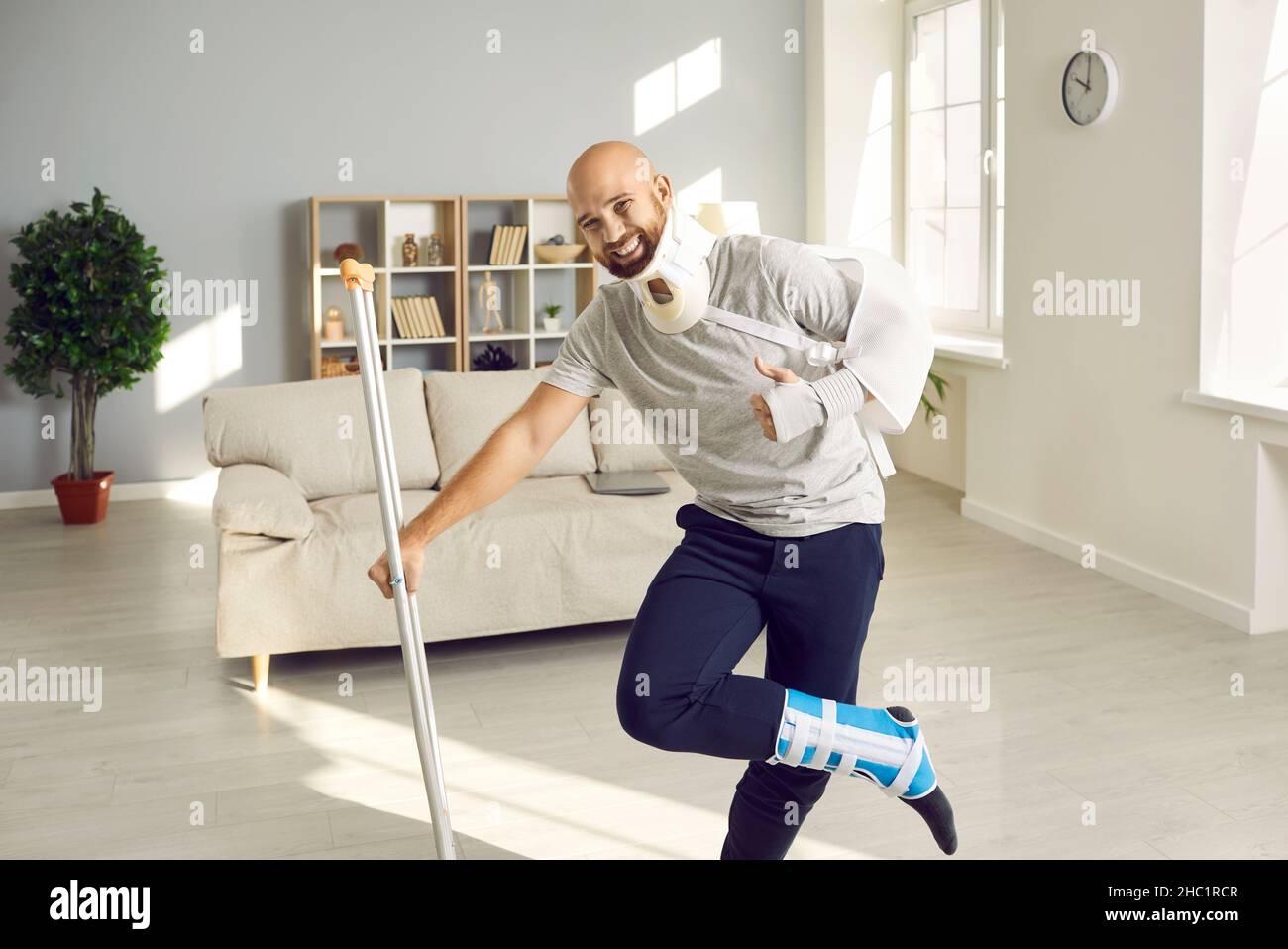 Happy man on sick leave due to injuries leaning on crutch, smiling and showing thumbs-up Stock Photo