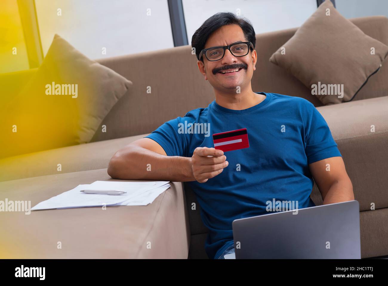 Middle age man shopping online through laptop using credit card while sitting on sofa Stock Photo