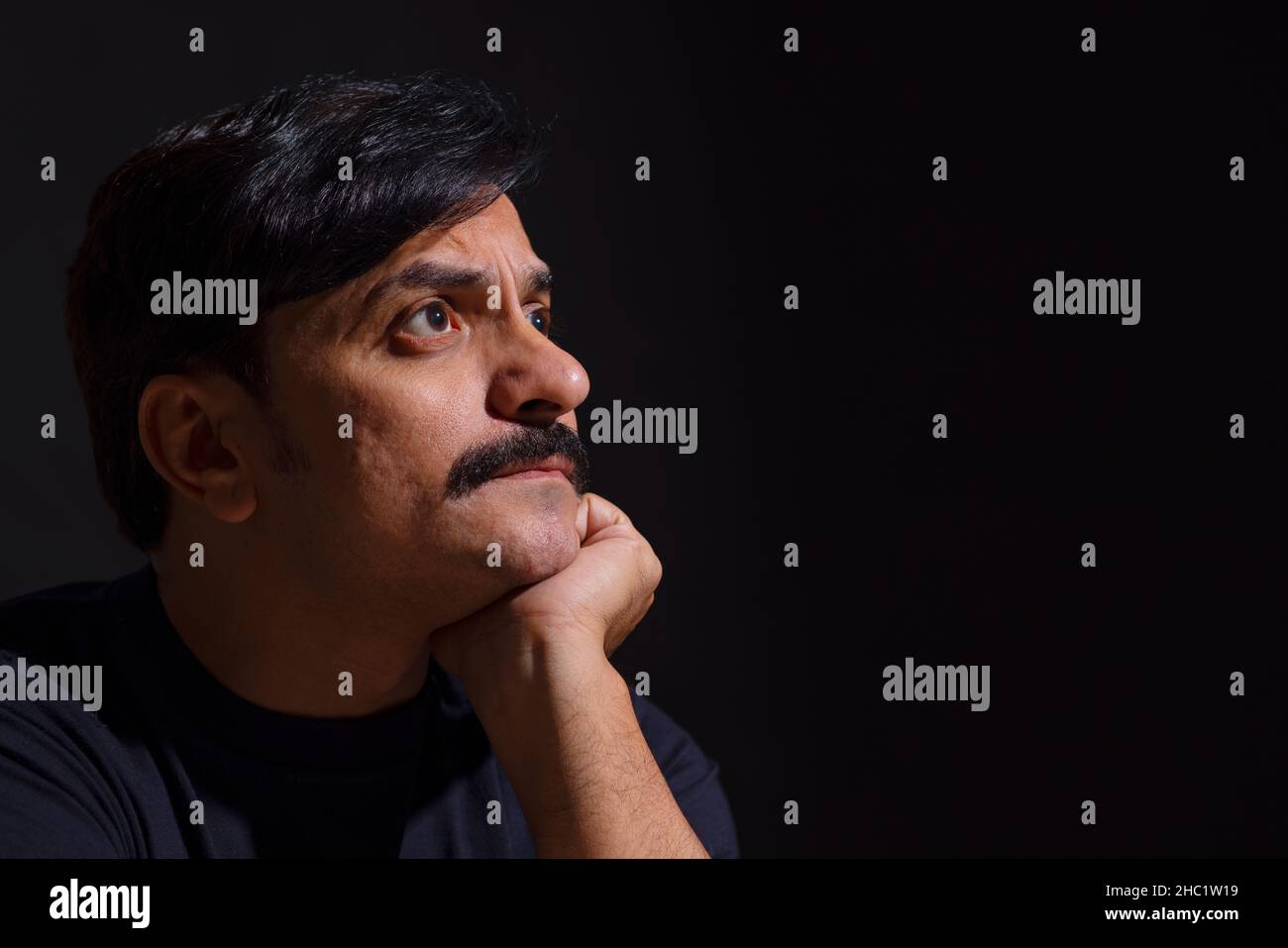 Side view of a common man with his hand on chin with black background Stock Photo