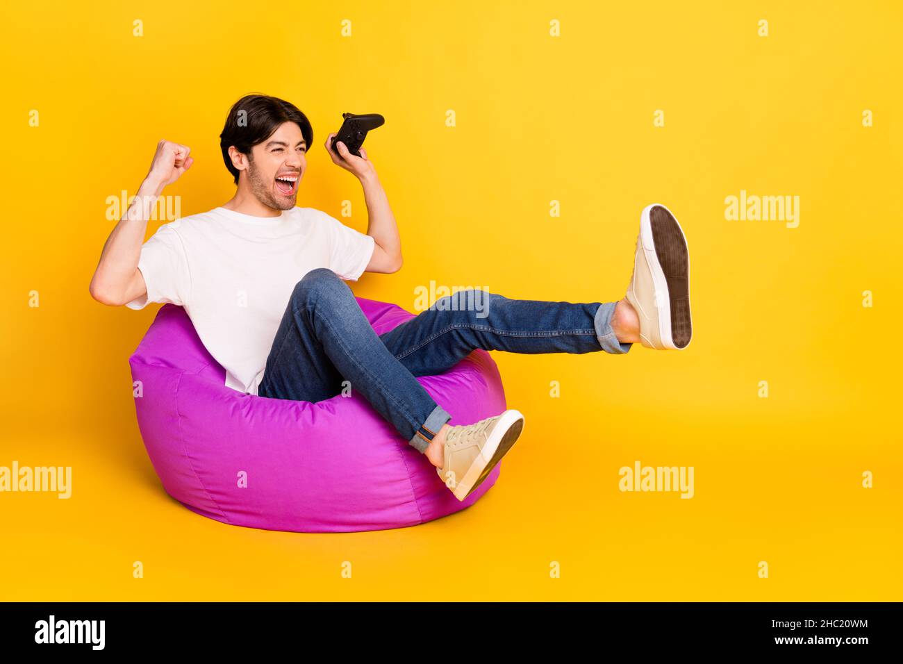 Portrait of attractive lucky cheerful guy playing game having fun rejoicing triumph isolated over bright yellow color background Stock Photo