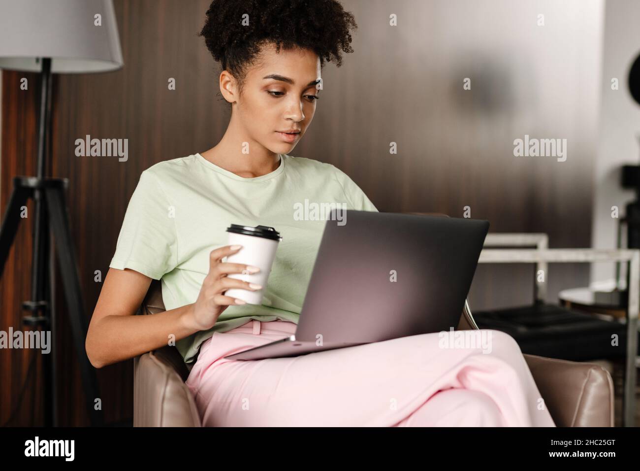 Young black woman drinking coffee while working with laptop at home ...