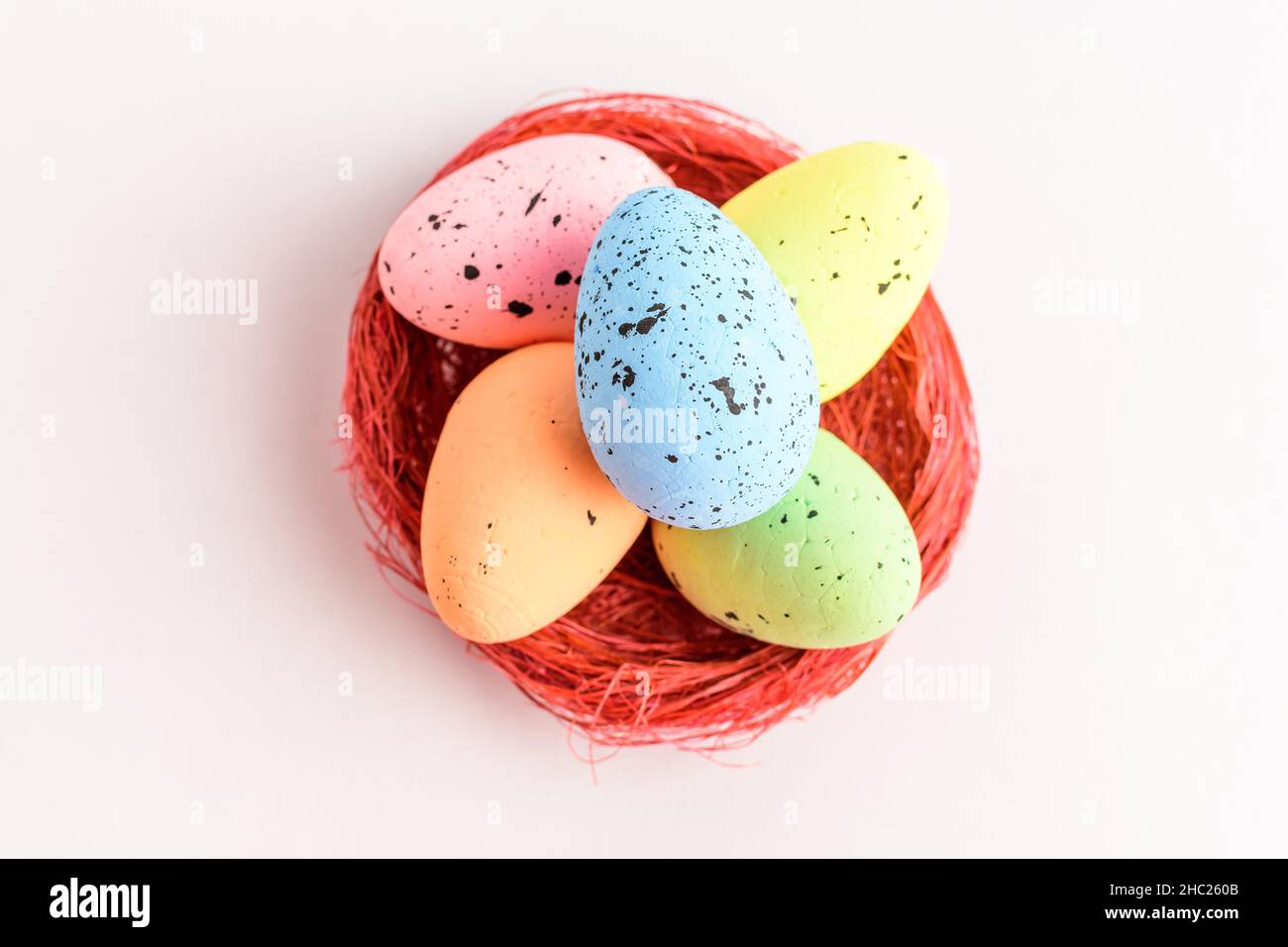 Mixed colored decorative red Easter eggs in a red rustic basket isolated on a white table Stock Photo